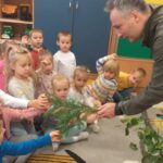 Pan Leśnik pokazuje dzieciom gałązki drzew liściastych i iglastych.