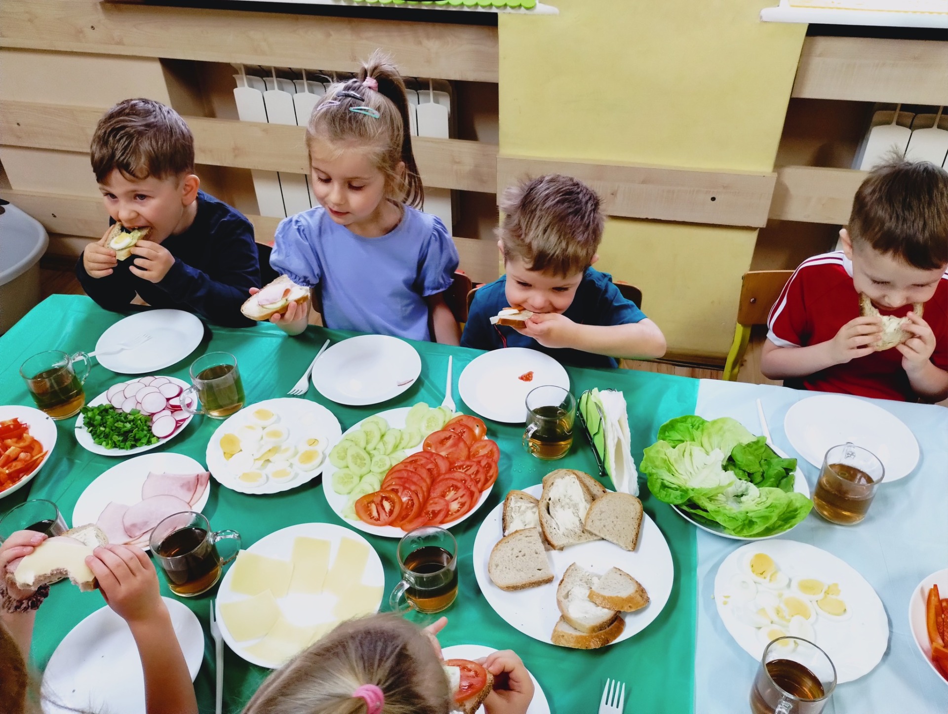 Dzieci przy stole, jedzą przygotowane przez siebie kanapki.