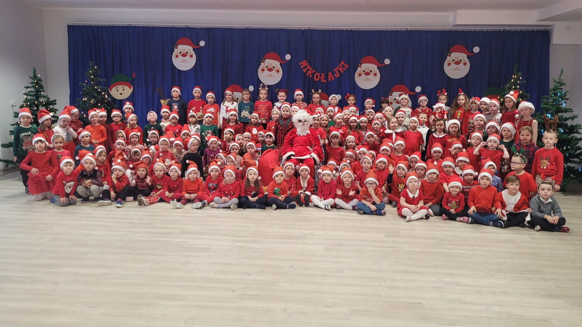 Wspólne zdjęcie wszystkich dzieci z Mikołajem. W tle mikołajkowa dekoracja.