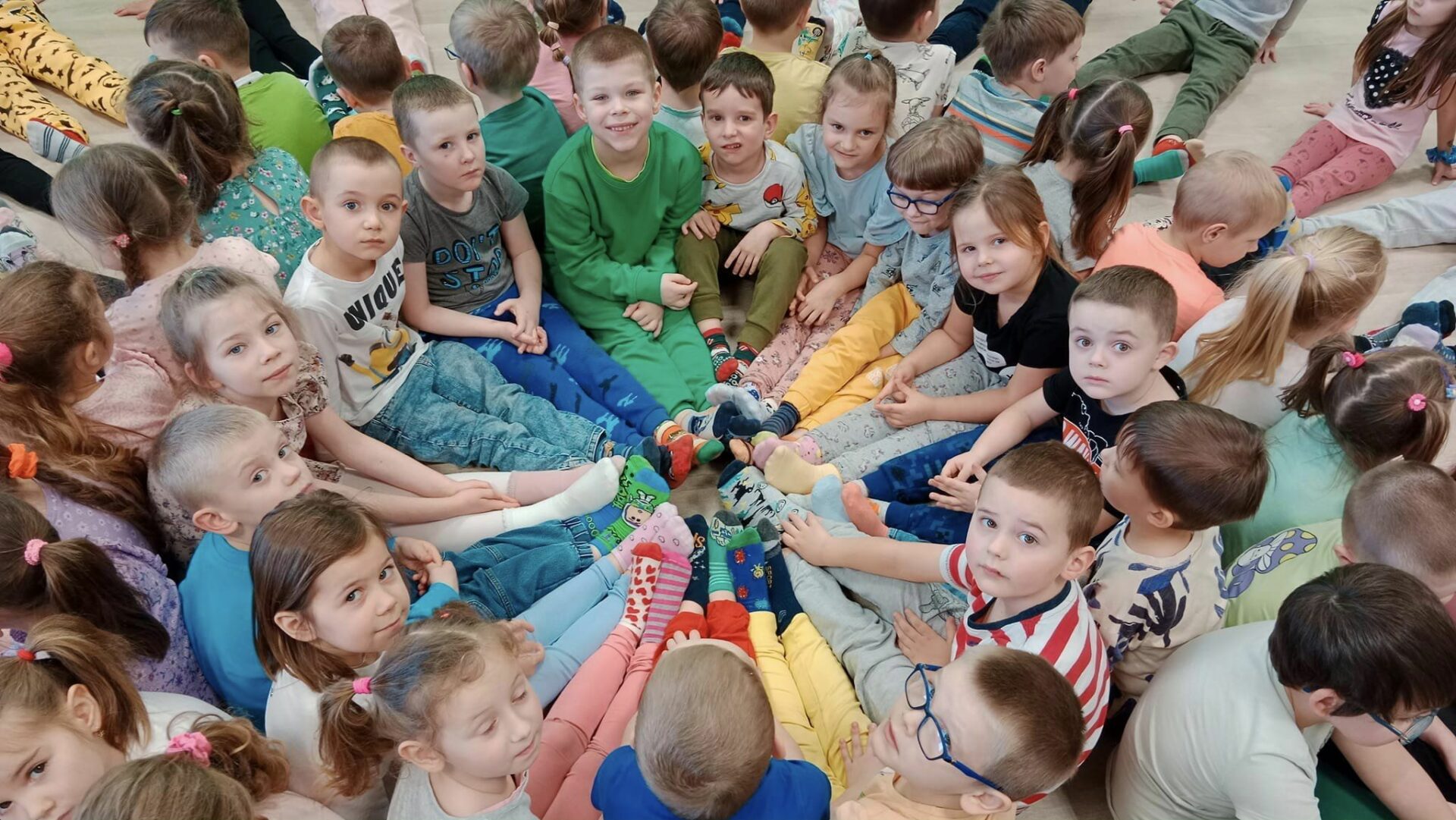 Dzieci w kółeczku na podłodze, demonstrują skarpetki nie do pary.