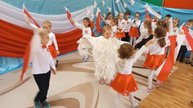 dzieci tańczące na tle biało-czerwonej dekoracji