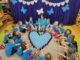 Dzieci w kręgu na podłodze, wokół serca ułożonego z niebieskich kubków.