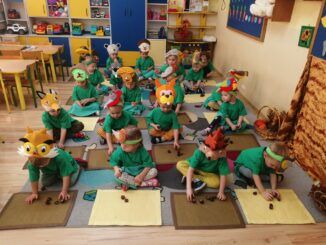 przedszkolaki w zielonych strojach rysują na kartkach