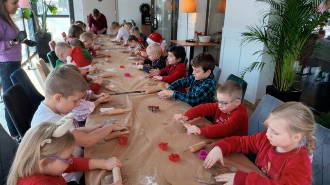Dzieci przy długim stole wałkują ciasto na pierniki.