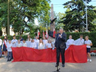 Na pierwszym planie Burmistrz Miasta, dalej dzieci z biało-czerwoną flagą, w tle pomnik ks. Brzóski